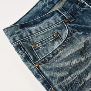 Detail of blue flare jeans with vintage wash, bronze rivets and artistic text print
