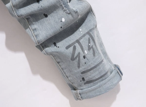 Close-up of blue distressed jeans featuring paint splatters and graphic print at the hem