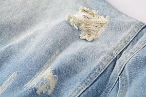 Macro shot of light wash denim showing distressed ripped details and double yellow stitching