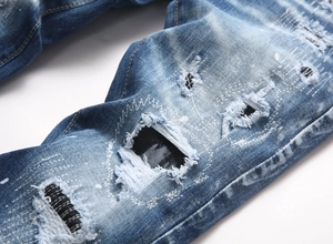 Detail of blue distressed denim with ripped patches, white paint splatters and repair stitching