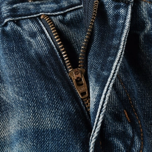 Macro shot of durable YKK metal zipper and vintage washed denim texture on men's flare jeans