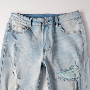 Detailed view of light blue distressed jeans with stripe patches and vintage button