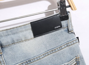 Detail of blue denim jeans featuring a black leather logo patch on the waistline