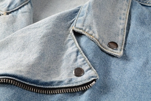 Close-up of light blue denim jacket collar with heavy wash and metallic rivet details