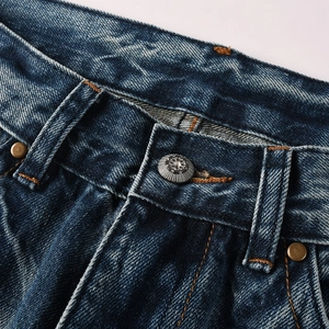 Close-up of vintage metal button and yellow stitching on dark blue washed flare jeans