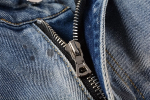 Macro detail of the metal zipper and yellow stitching on light blue distressed jeans