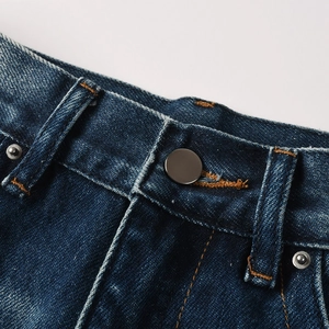 Detail of waist area on dark blue flare jeans featuring contrast stitching and metal button