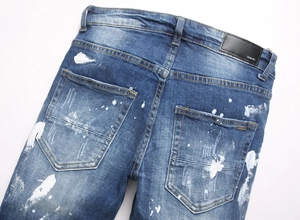 Detail shot of blue denim jeans featuring paint splatter effect and leather back label