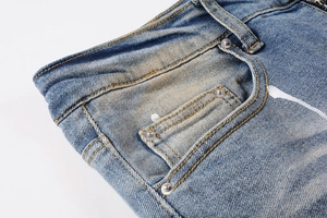 Macro detail of washed denim jeans showing orange stitching and white paint splatter style