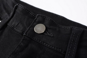 Makro-Detail von schwarzem Denim-Bund mit silbernem Metallknopf und präzisen Nähten
