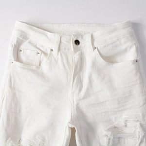 Detail view of white ripped denim jeans waist with metal button and rivet accents