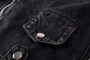 Close-up of black denim jacket pocket with silver metal button and zipper detailing