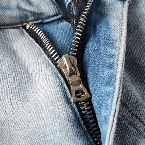 Detailed close-up of a silver metal zipper on light blue washed denim pants for men