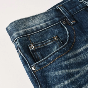 Close-up of dark blue heavy denim fabric showing side pocket and metal rivet details