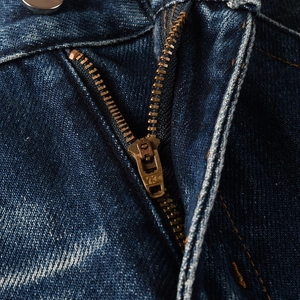 Macro detail of dark blue denim jeans featuring a vintage copper YKK metal zipper fly