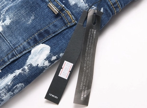 Detail of blue denim with white splash paint effect and branded metal logo hardware