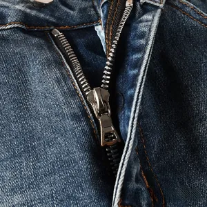Gros plan sur la fermeture éclair en bronze et le bouton du jean denim bleu foncé