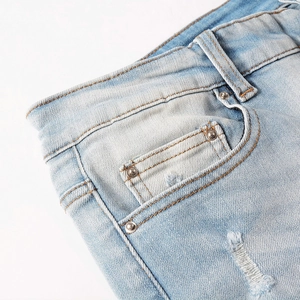 Close-up of light blue distressed denim jeans with orange stitching and metal rivets