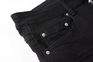 Detail view of black denim jeans waist with silver metal rivets and twill texture