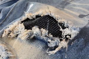 Detail of distressed blue jeans with ripped holes, black mesh lining, and beadwork accents