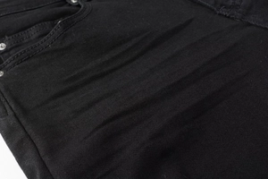 Macro shot of black denim texture with whiskers wash effect and silver metal rivets details