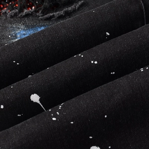 Macro detail of distressed black denim with white paint splatters and red rhinestones