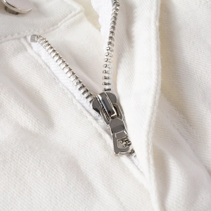 Close-up detail of silver metal zipper and button on white slim fit stretch denim pants