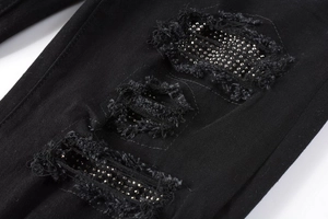 Close-up of distressed black denim with rhinestone detailing and ripped fringe textures