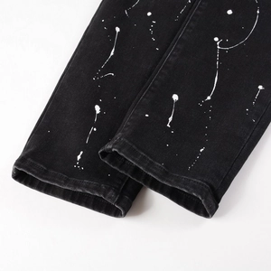 Men's black distressed jeans featuring artistic white paint splatter and cuffed hem detail