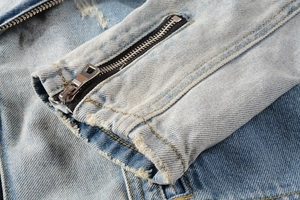 Detail of light blue denim jacket sleeve featuring metal zipper and distressed worn edges