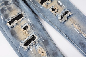 Close-up of washed blue denim with distressed rips, black mesh lining and paint splatter