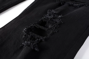 Macro view of distressed denim fabric with ripped details and white fringe on black jeans
