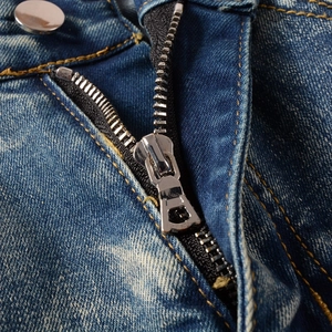 Detail of high street biker jeans featuring a metallic zipper and silver button closure