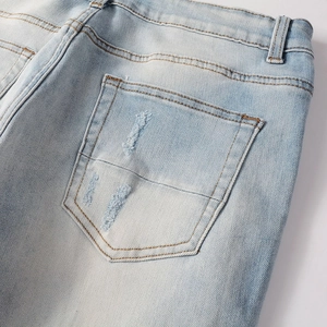 Detailed close-up of light blue denim back pocket with distressed rips and washed texture