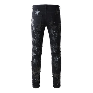 Detail view of black slim jeans featuring leather star patches and washed denim texture