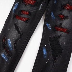 Men's slim black ripped jeans featuring red rhinestone patches and blue paint splatter