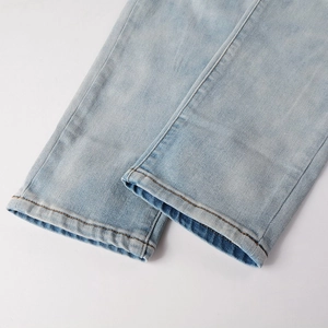 Close-up of light blue distressed denim jeans cuff with orange contrast stitching details