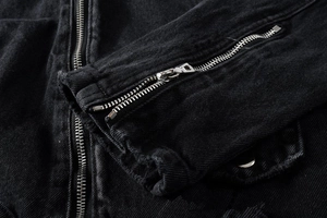 Detail of metal zipper and frayed edges on black washed denim jacket sleeve cuff