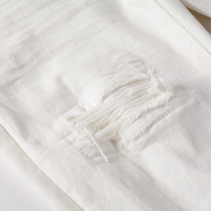 Detailed close-up of distressed white denim jeans with ripped horizontal fraying edges