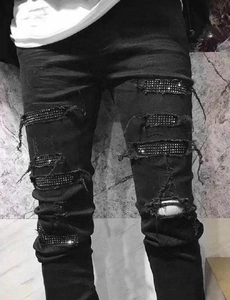Detail of men's slim black ripped jeans featuring sparkling silver rhinestone inserts