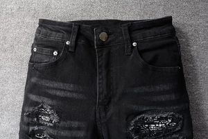 Detail of black distressed denim jeans featuring paisley patchwork and metal button closure