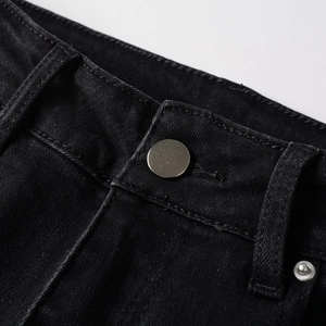 Detailed macro view of the waistband area on black denim jeans with silver metal button