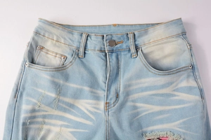 Detail of light blue distressed jeans with whiskers and pink floral pattern patches