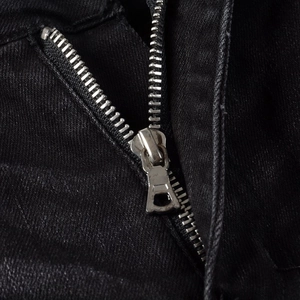 Detailed close-up of a high-quality silver metal zipper on heavy black denim fabric