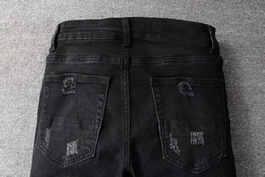 Detailed view of back pockets on black distressed denim jeans with frayed hole design