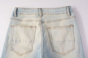 Detailed back pocket view of distressed light blue denim jeans with yellow stitching