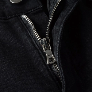 Macro shot of silver metal zipper and button detail on black slim fit denim jeans