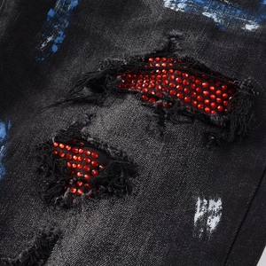 Macro detail of men's distressed jeans with red rhinestones and artistic paint splatter