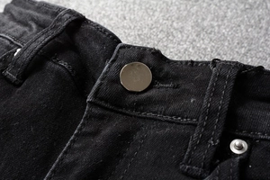 Detail shot of a silver metal button and reinforced stitching on black denim jeans