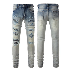 Detail of distressed light blue slim jeans featuring ripped patches and street style prints